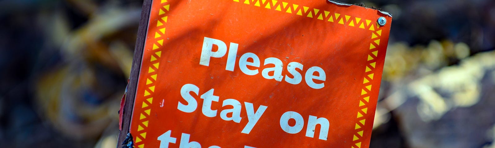 orange sign that reads “Please Stay on the Path”