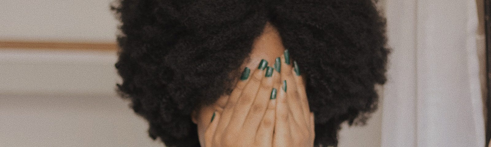 Black woman covering her face with her hands.