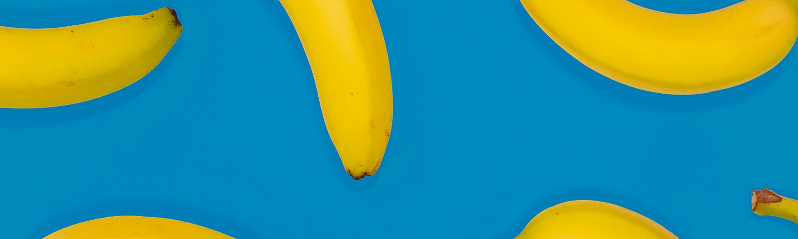Blue background with many bananas spread around. It looks like they are falling from the sky.
