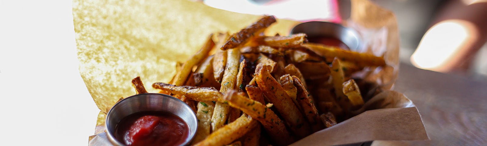 Crispy french fries in a metal basket lined with brown paper and a a small dish of ketchup.