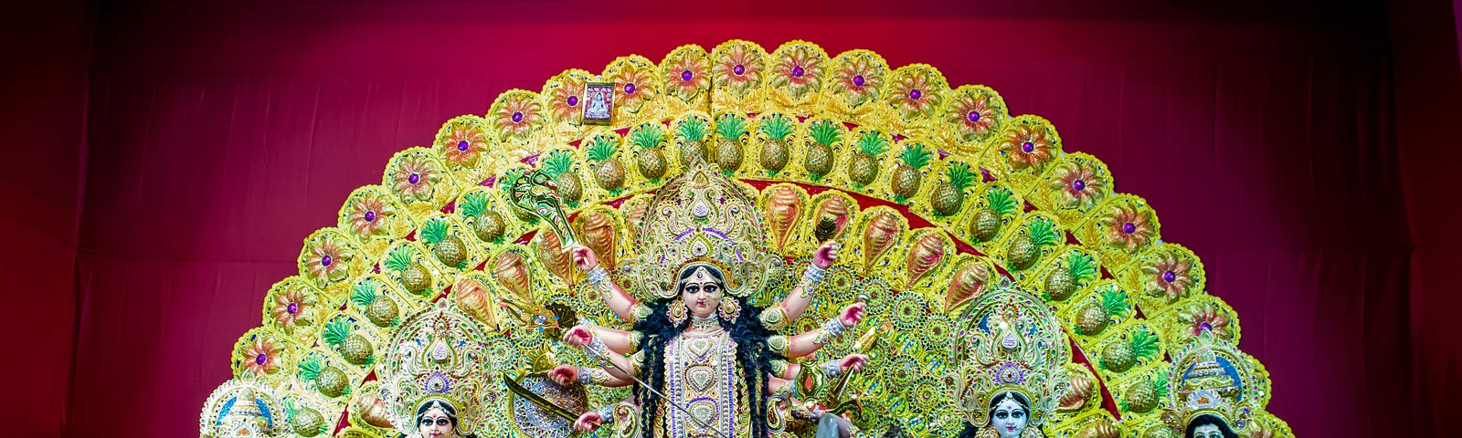 An Indian Goddess against a colorful backdrop with her 4 children standing on either side of her.