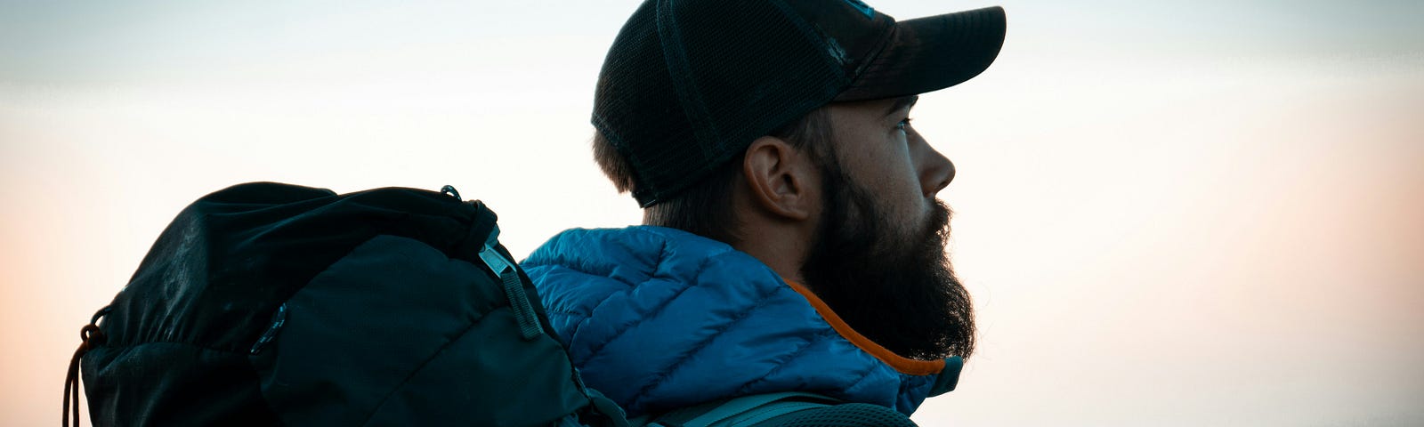 A young, bearded hiker with backpack stares into the distance