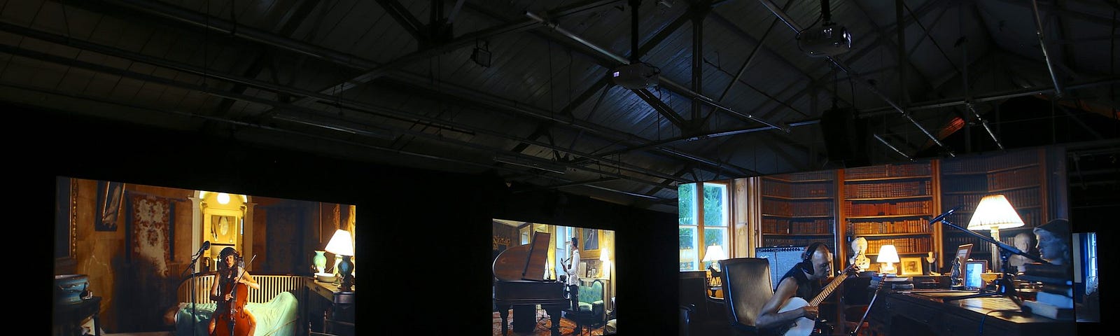 Blacked out room hosting several large projector screens showing musicians playing alone in separate rooms.