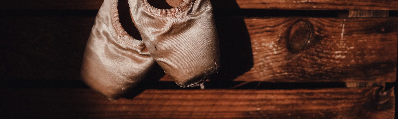 Worn pointe ballet shoes on a dark wood backdrop