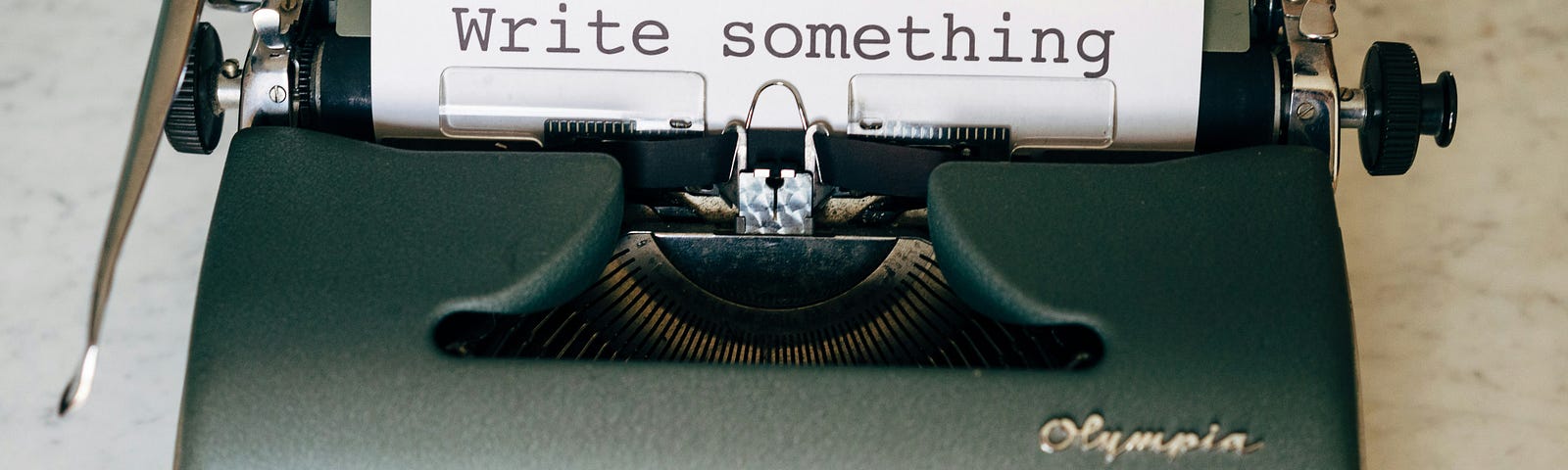 An antique typewriter with a sheet of paper inside that says “Write Something”