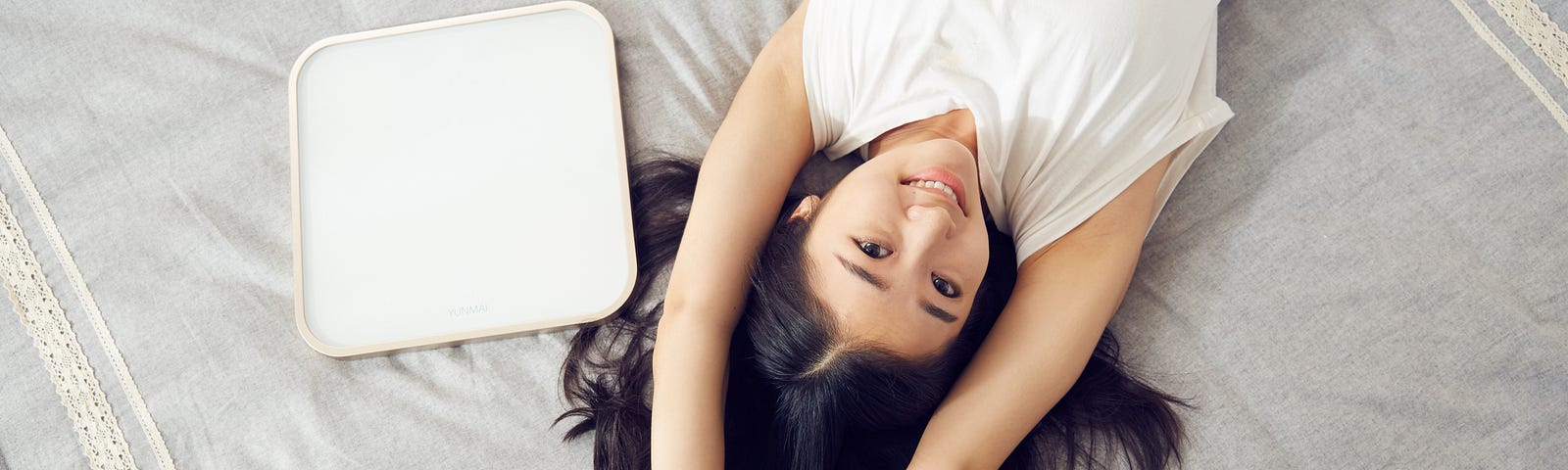 woman lying on her back on a bed with arms over her head, smiling