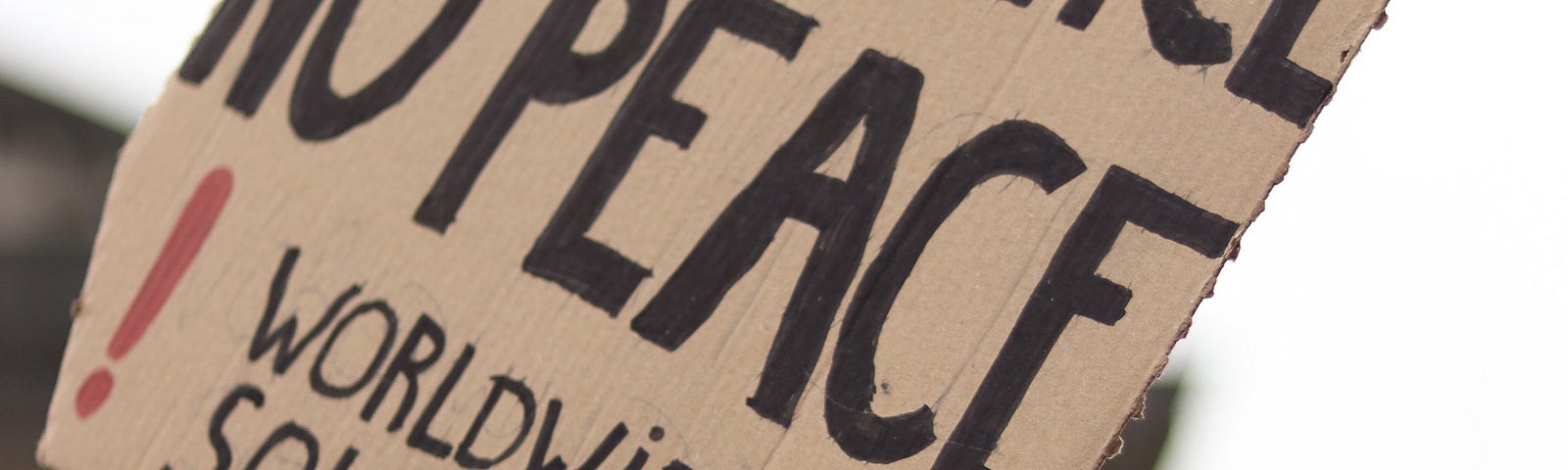 A cardboard sign help up at a protest. It reads “No Justice, No Peace. Worldwide Solidarity.”