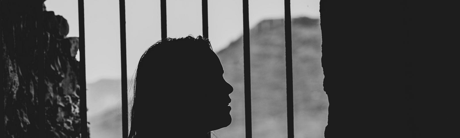 Silouette of woman standing in front of prison bars.