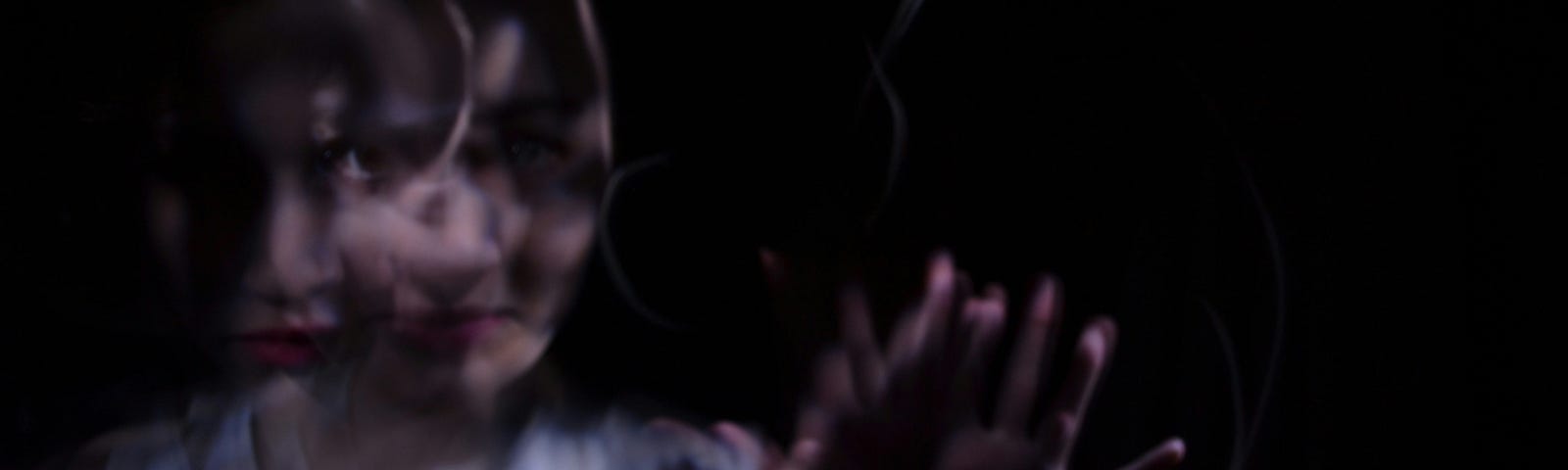 A blurry and distorted image of a woman reaching through the dark