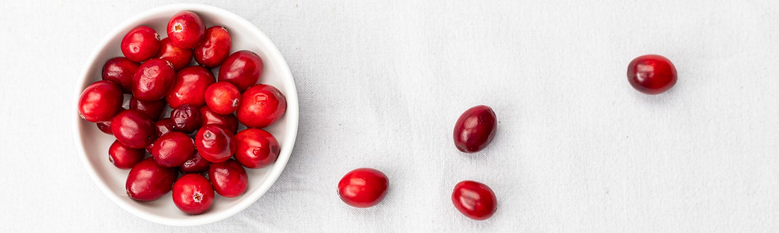 A small white bowl (in the upper left) has a couple dozen crnanberries in it. Six additional cranberries are scattered on the right side of the image. Upwards of 50 to 60 percent of women will have at least one UTI in their lifetime. Men can get UTIs, too. Today we explore how you can supercharge your health. Recent studies have found that cranberry products can prevent urinary tract infections.