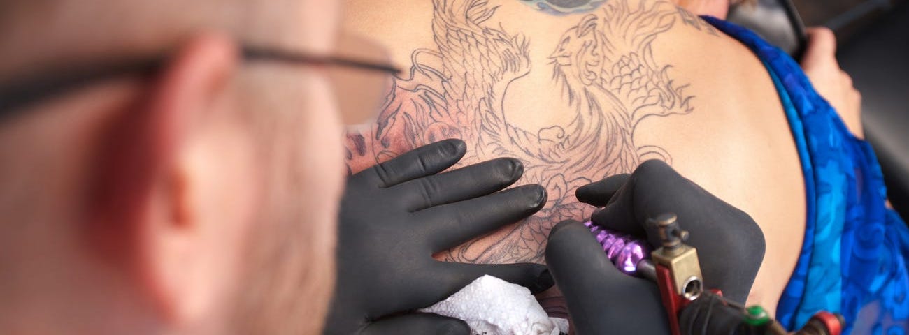 A tatto artist inks an individual’s back.