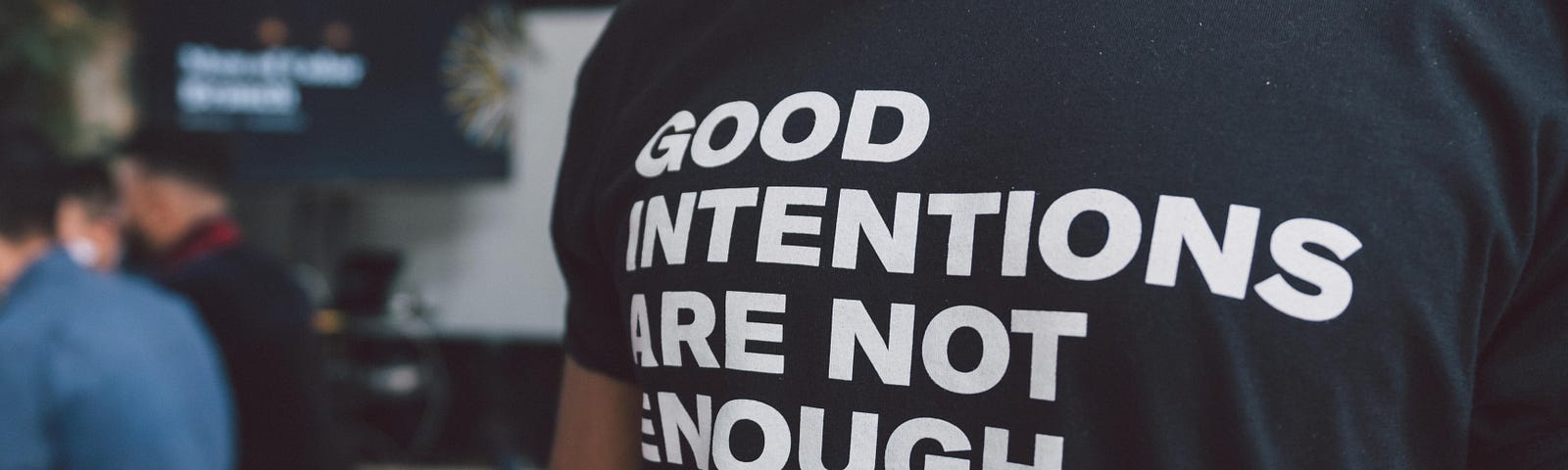 This is a photo of a person wearing a tshirt that says “good intentions are not enough”
