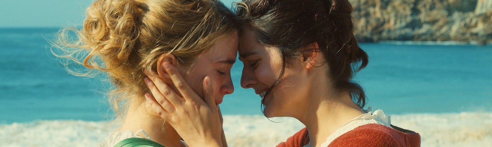 Two white women embrace on a beach.