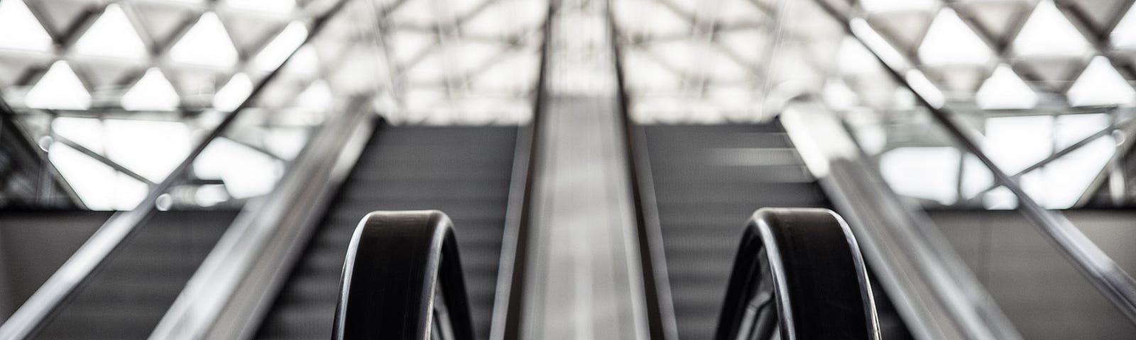 Black and white photo of escalators with a geometric structure behind them.