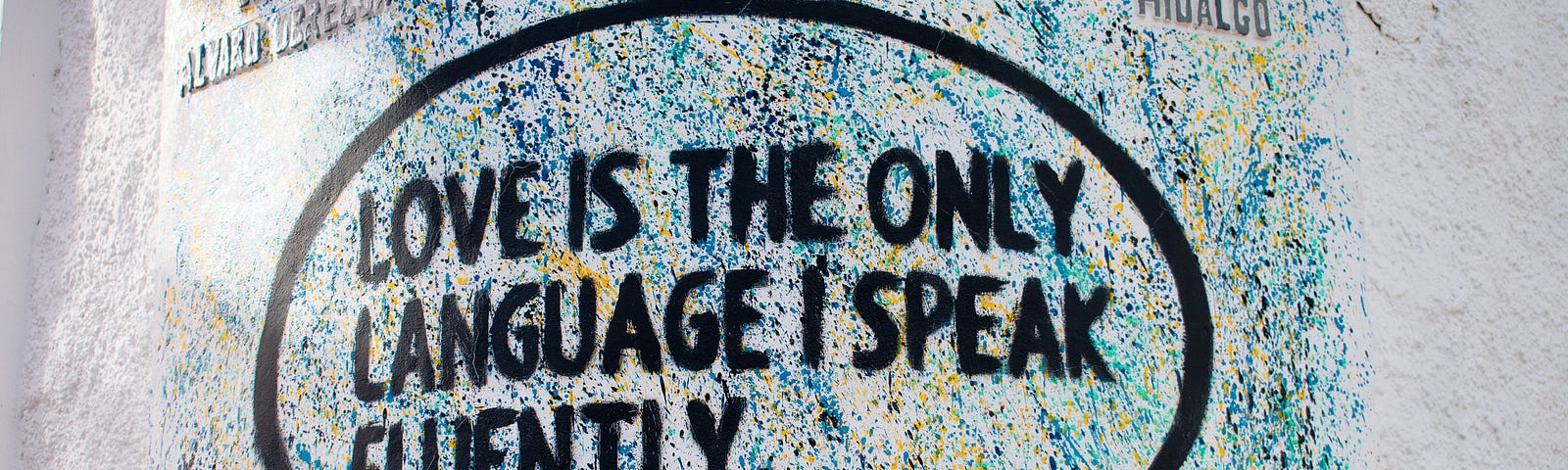 Graffiti on a wall showing a speach bobble saying “Love is the only language I speak fluently.”, signed by TrystyScribe
