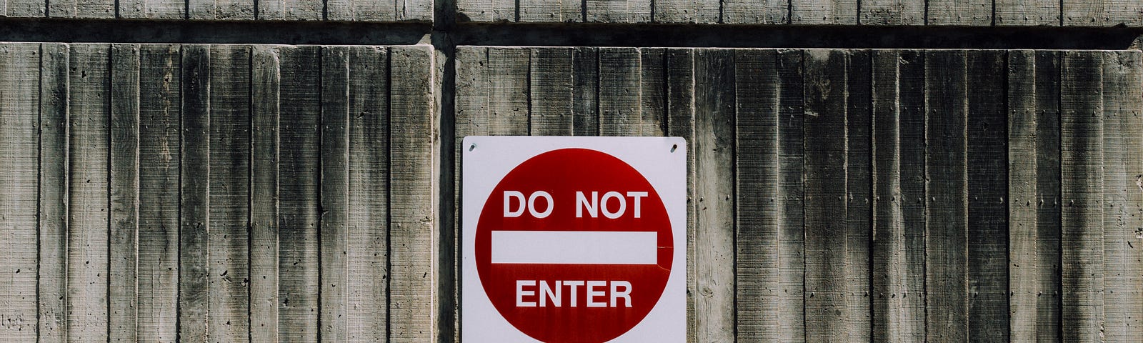 On a wooden wall is a red and white “Do Not Enter” sign.