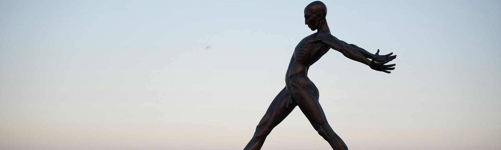 Statue of someone stepping off a wall into the sea