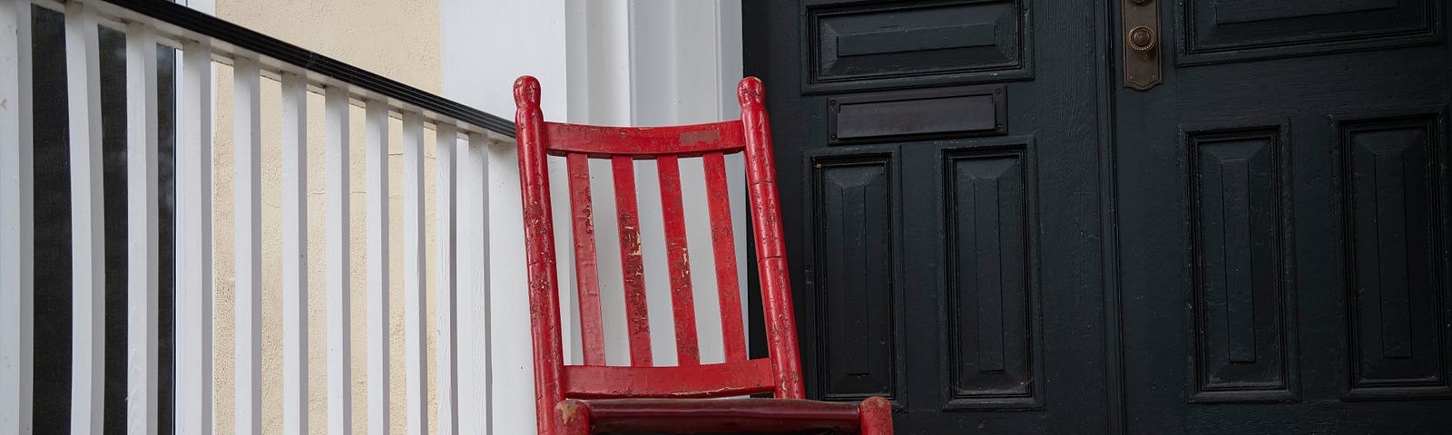 red rocking chair in front of black doors, next to a black and white railing