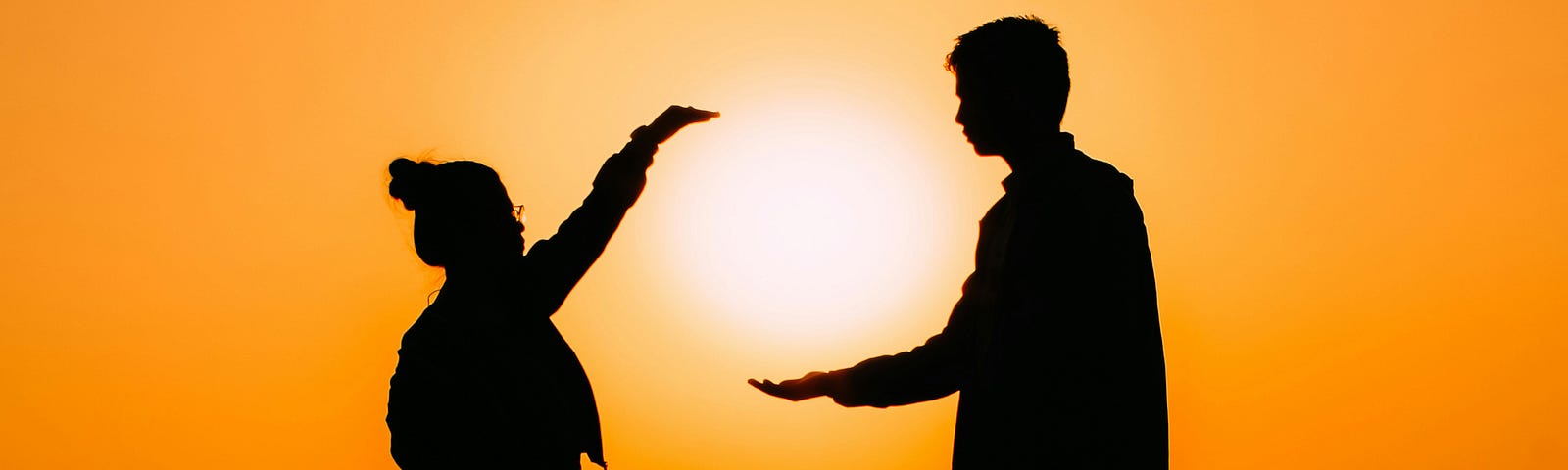 a woman and man framing the sun with their hands