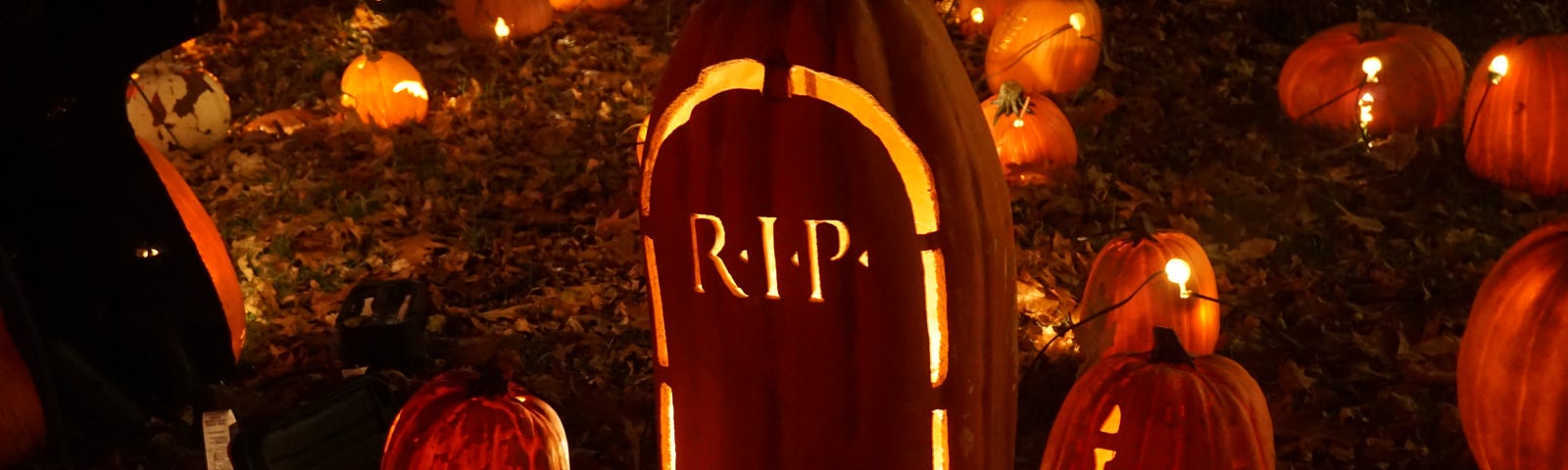 Three carved pumpkings, lit up at night. The middle one says RIP.