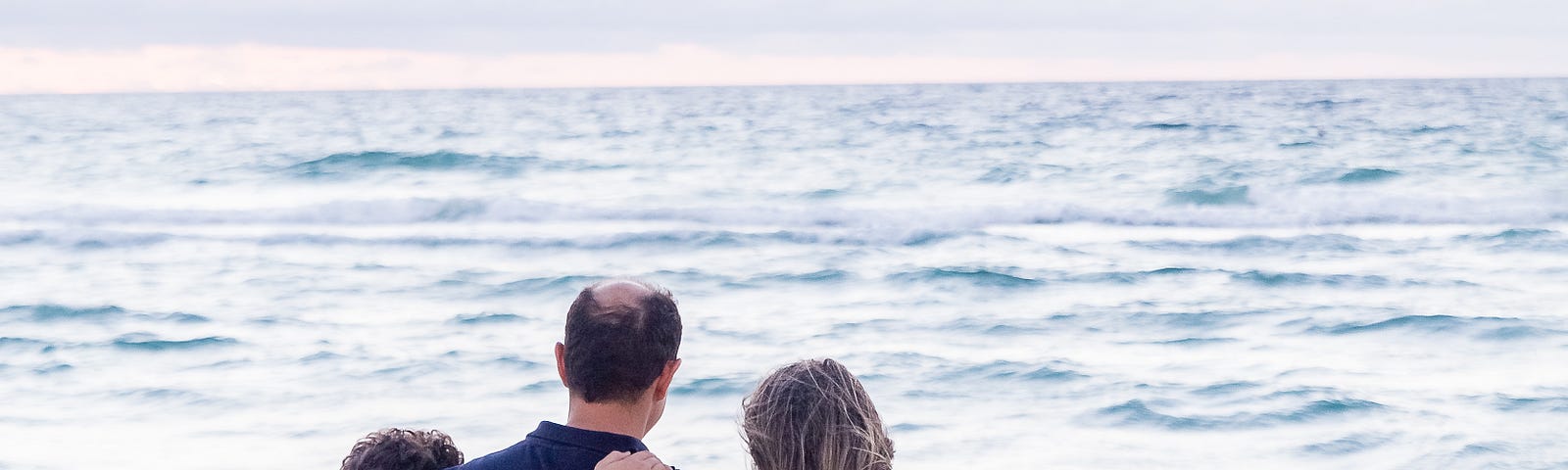 Rear view of family with their arms around each other by the beach