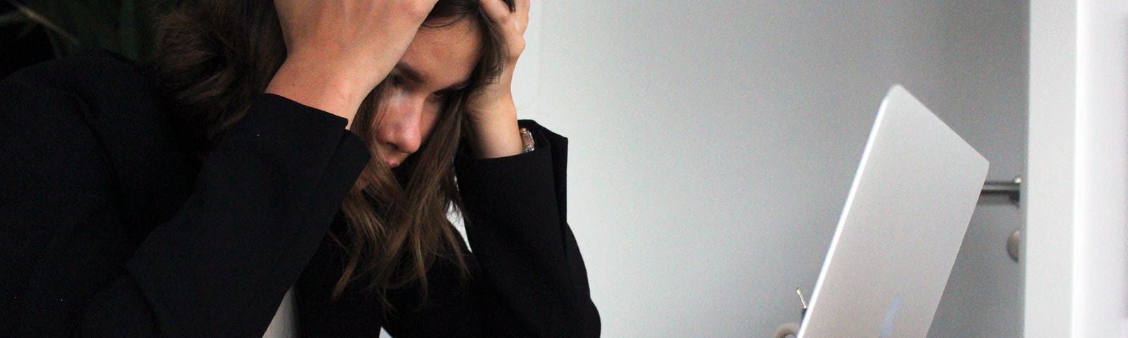 A younger woman with her head in her hands, staring at a laptop computer. She has removed her eyeglasses.