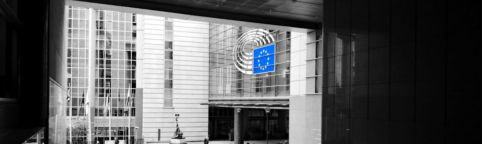 Black and white image of the entrance to the European Parliament building with the European Union flag which is tho only item in colour.
