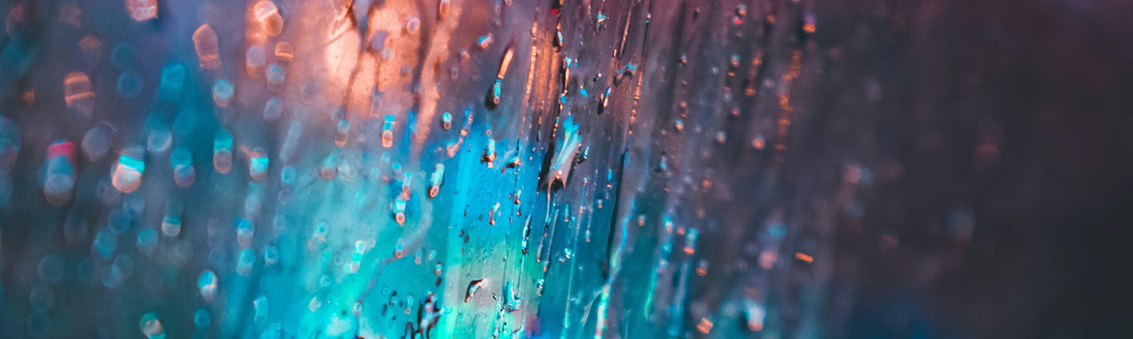 Blue and pink lights are seen behind a fogged-up window with water droplets and condensation on it.