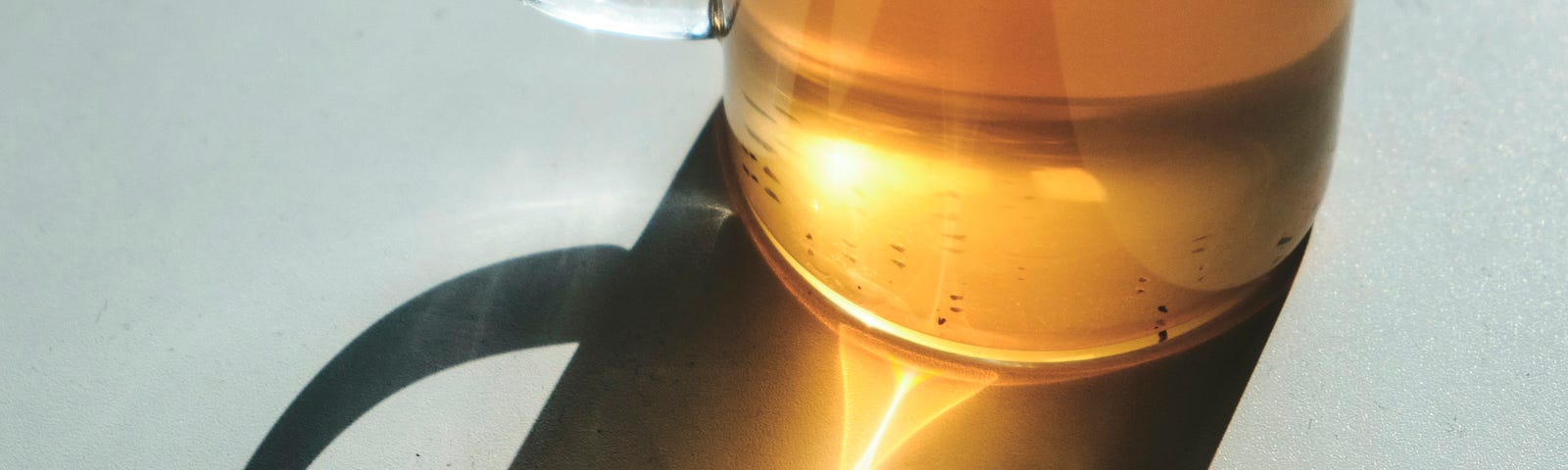 Golden tea filling a glass tea cup with the sun shining through it