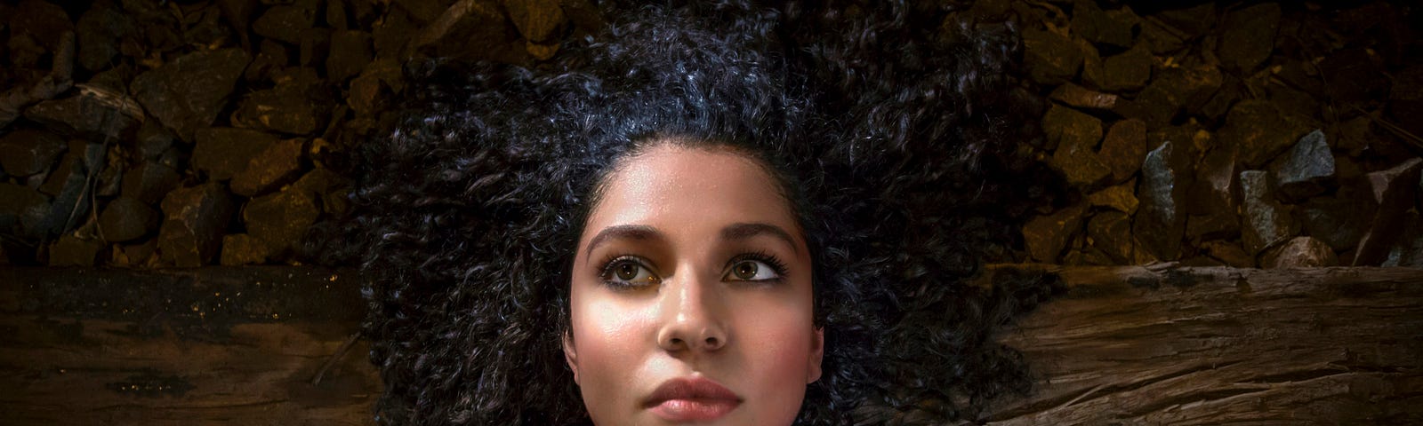 A young girl lying on the ground gazing with a lost look from the corner of the eye.