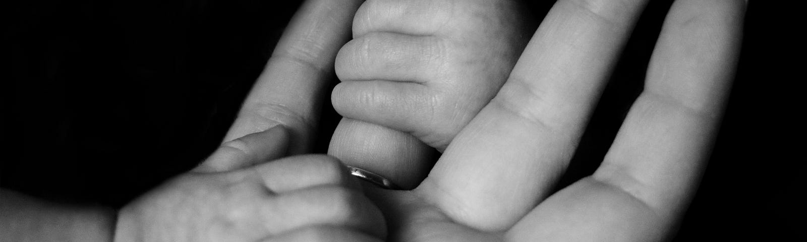 A baby grasping the hands of its father