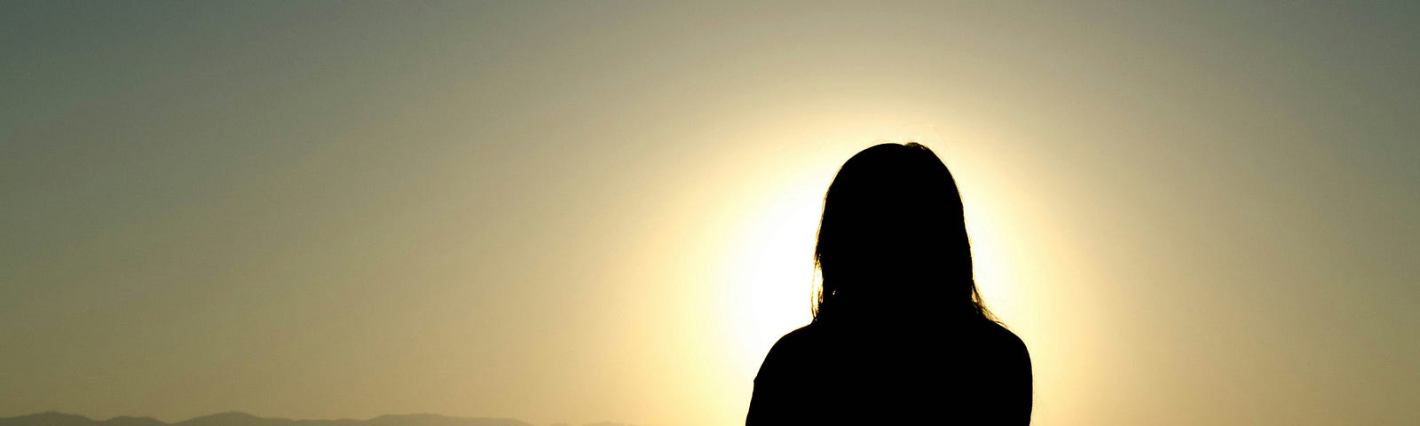 A silhouette of a person meditating in a seated position with the sun setting behind them.