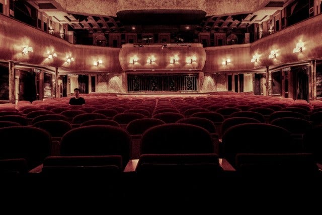 Lit empty theater from stage perspective with only one seated person near the back left side
