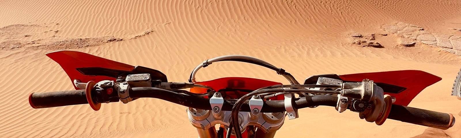 A picture of the desert taken from the driver of a motorcycle. The bike is standing on a dune with the endless sand before it.