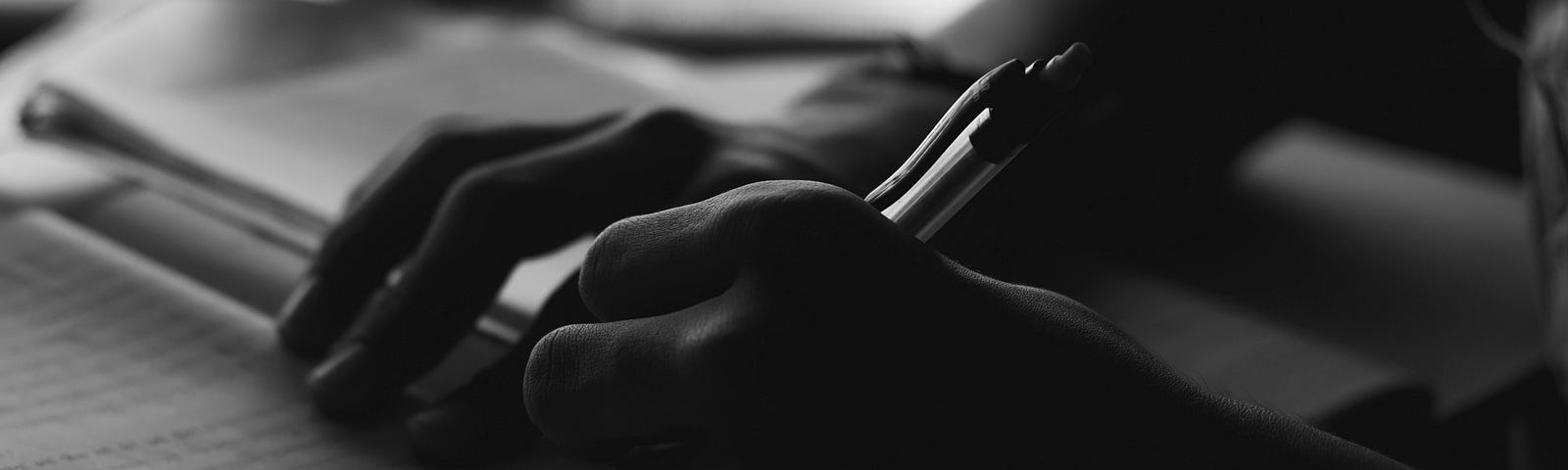 A black and white photo of a person’s hands holding a pen and writing in a notebook.