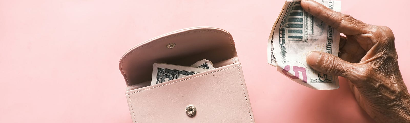 Pink back. The hands of an older person holding a pink leather coin purse. The left hand holds the purse with one dollar partially showing with the right hand getting ready to put $5 in the coin purse.
