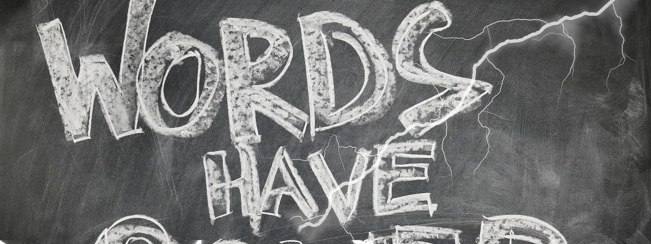 A blackboard with white block letters in chalk that say “Words Have Power.”