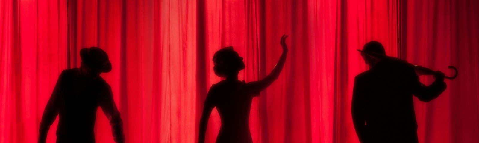Silhouettes of three actors behind a red, theater curtain. A man in a hat, a woman with an arm lifted, and another man with an umbrella.