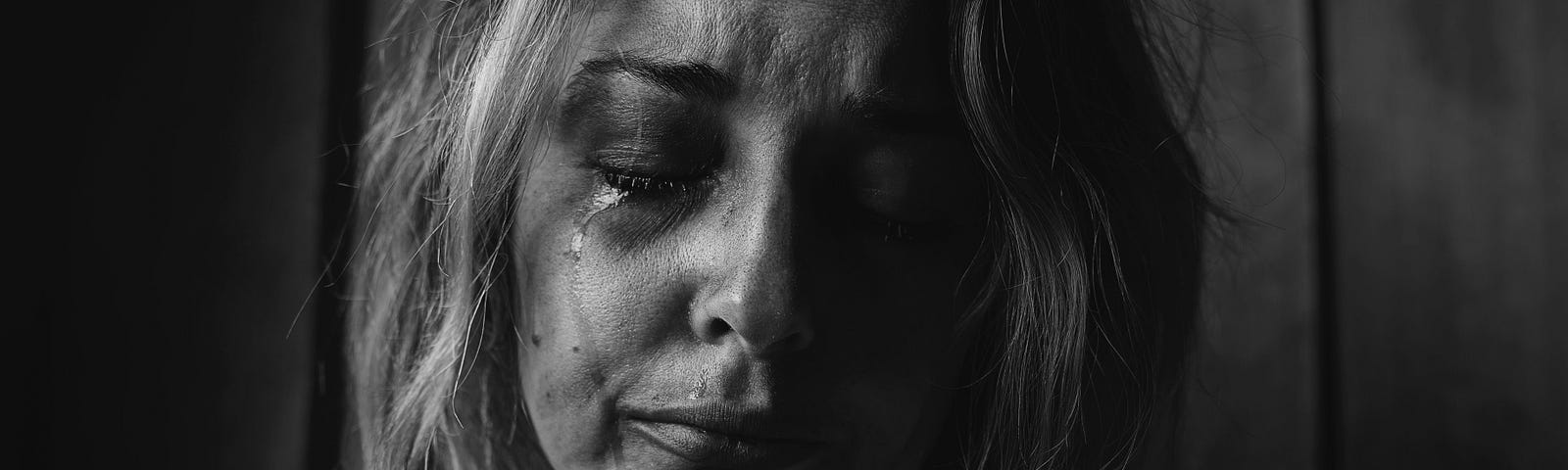 Black and white photo of a blond woman crying with tears rolling down her face.