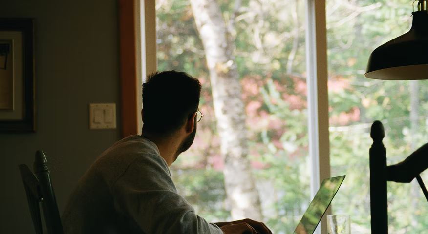 Homem sentado em frente ao notebook olhando pela janela home office — como instalar o maven no mac