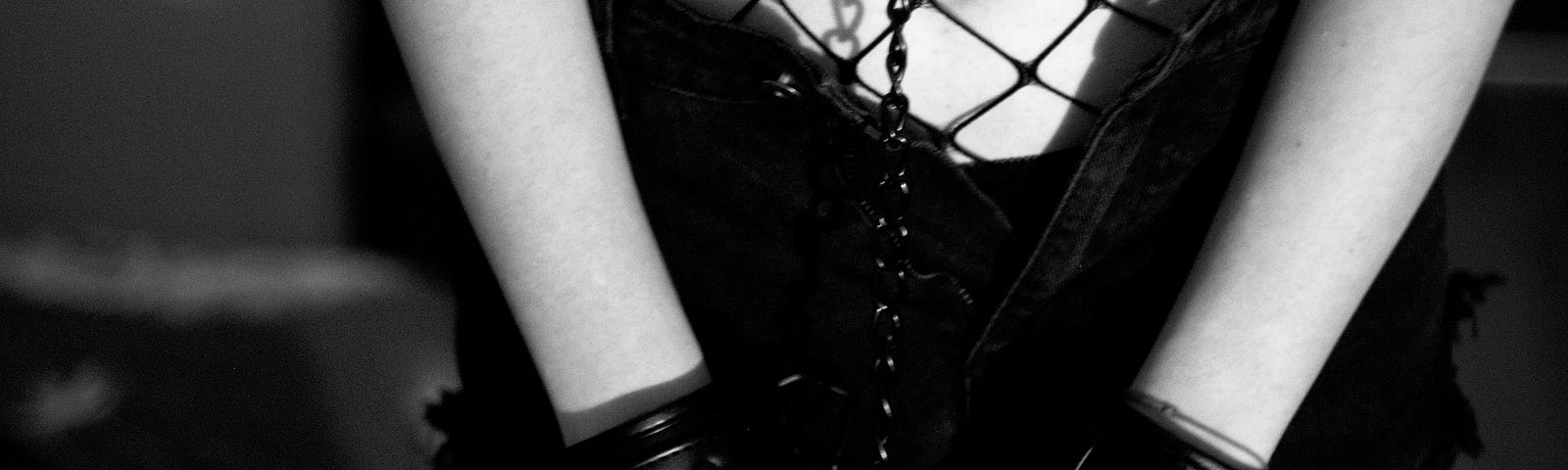 A woman wearing leather handcuffs and sexy black fishnet lingerie.