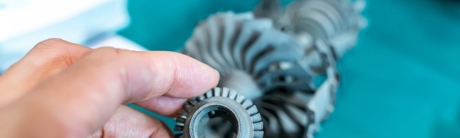 Photo of a hand holding a 3D printed gear over a 3D printed machine.