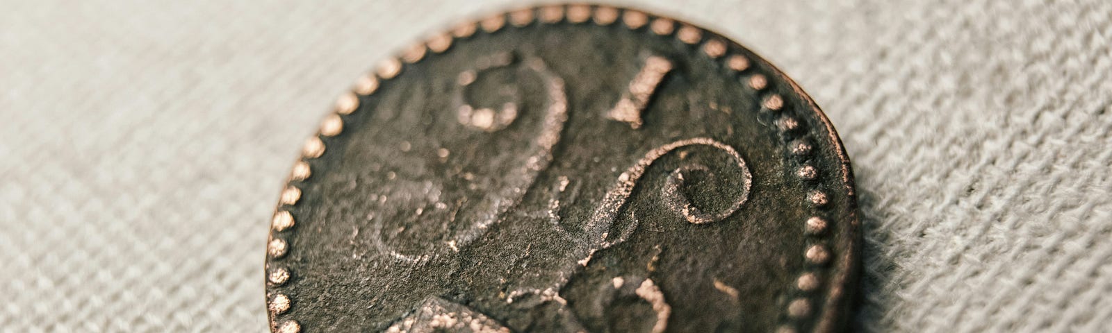 an antique coin with an unrecognizable ancient symbol on it. It is placed on a cloth backdrop.