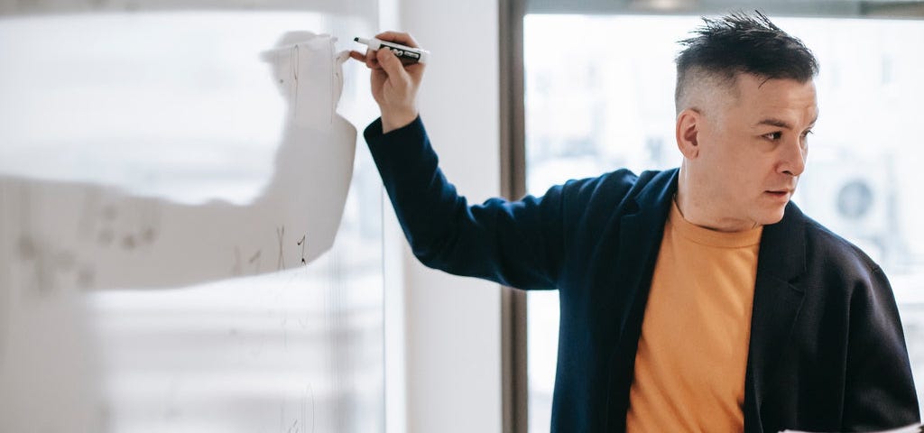 a man presenting as he writes in a whiteboard