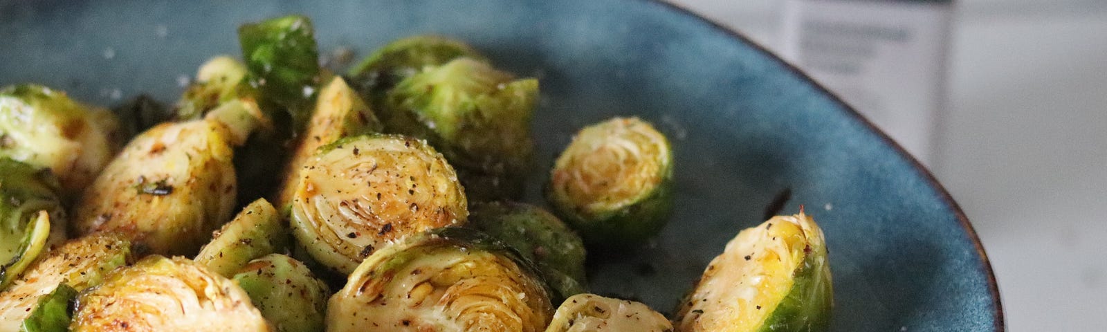 A picture of a blue plate full of sliced brussel sprouts sprinkled with salt and pepper and drizzled with oil.