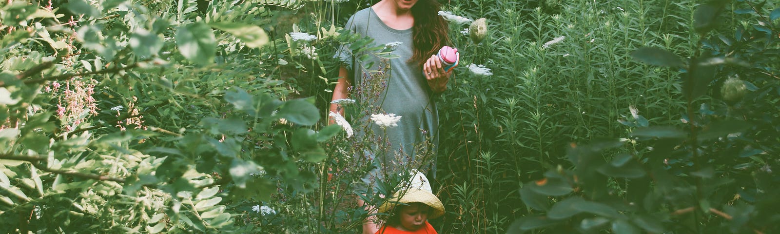 A mother accompanying her young child as he walks in a garden.