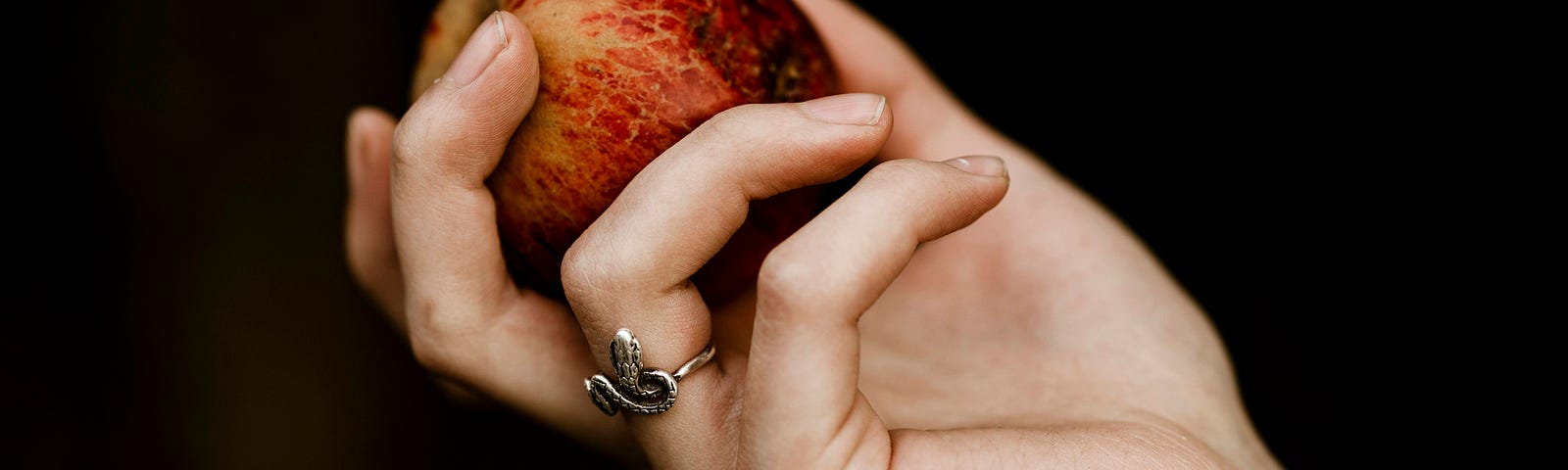Woman holding a red apple with a snake ring on her finger