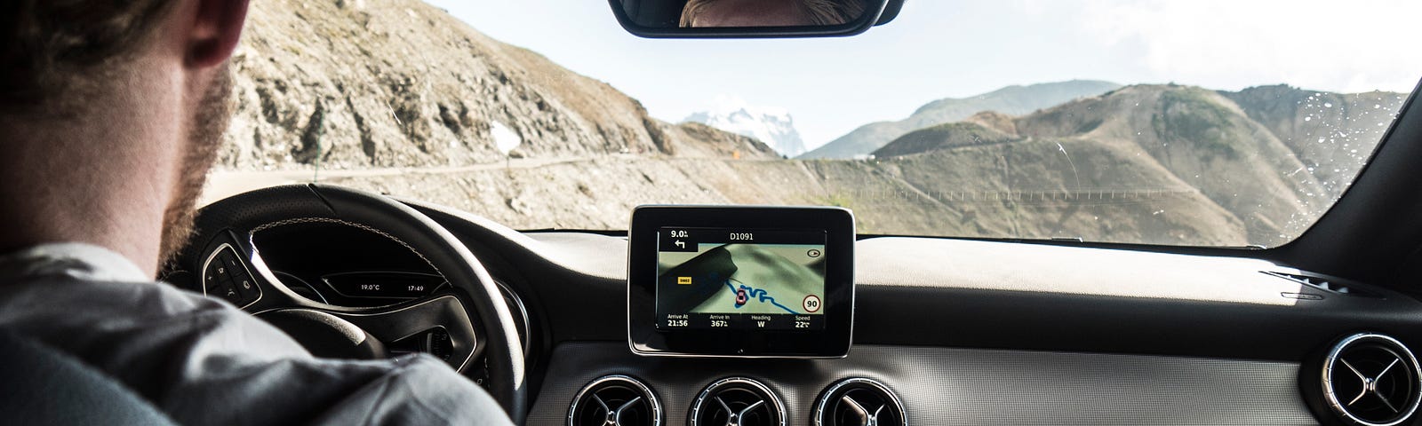 Point of view shot of man sitting in the driver’s seat of a car driving along the edge of a mountain.