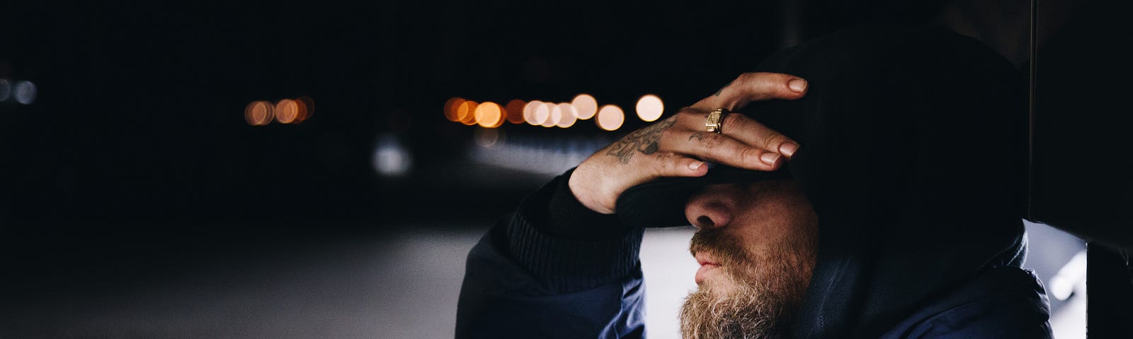 Photo of a man sitting on the ground outside at night with his head in his hand.