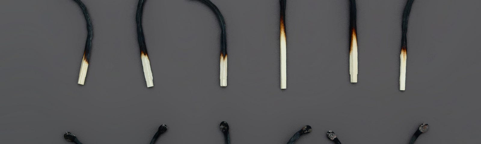 Two rows of matches burned about two thirds of the way down. They are laid out and bent in various directions against a charcoal gray background.